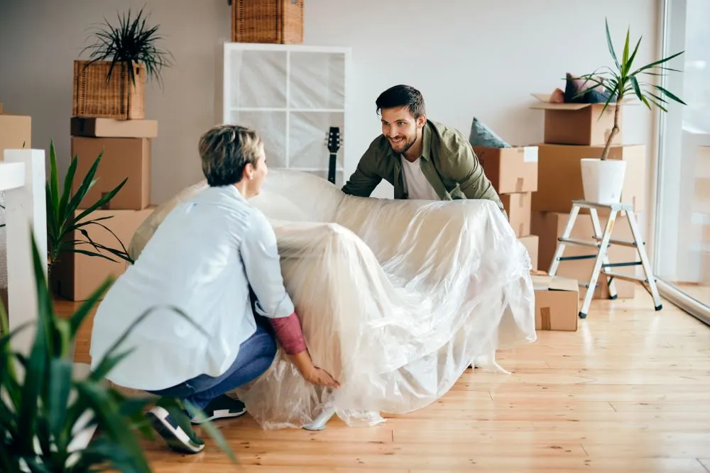 Deux personnes installent un canapé dans un logement meublé entouré de cartons de déménagement.
